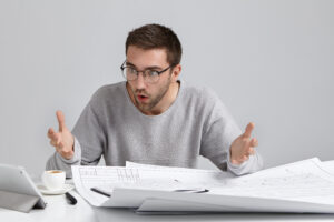 Horizontal portrait of puzzled male designer stares at screen of laptop, feels worried as realizes his fault, gestures in bewilderment, being annoyed. People, occupation, job, design concept